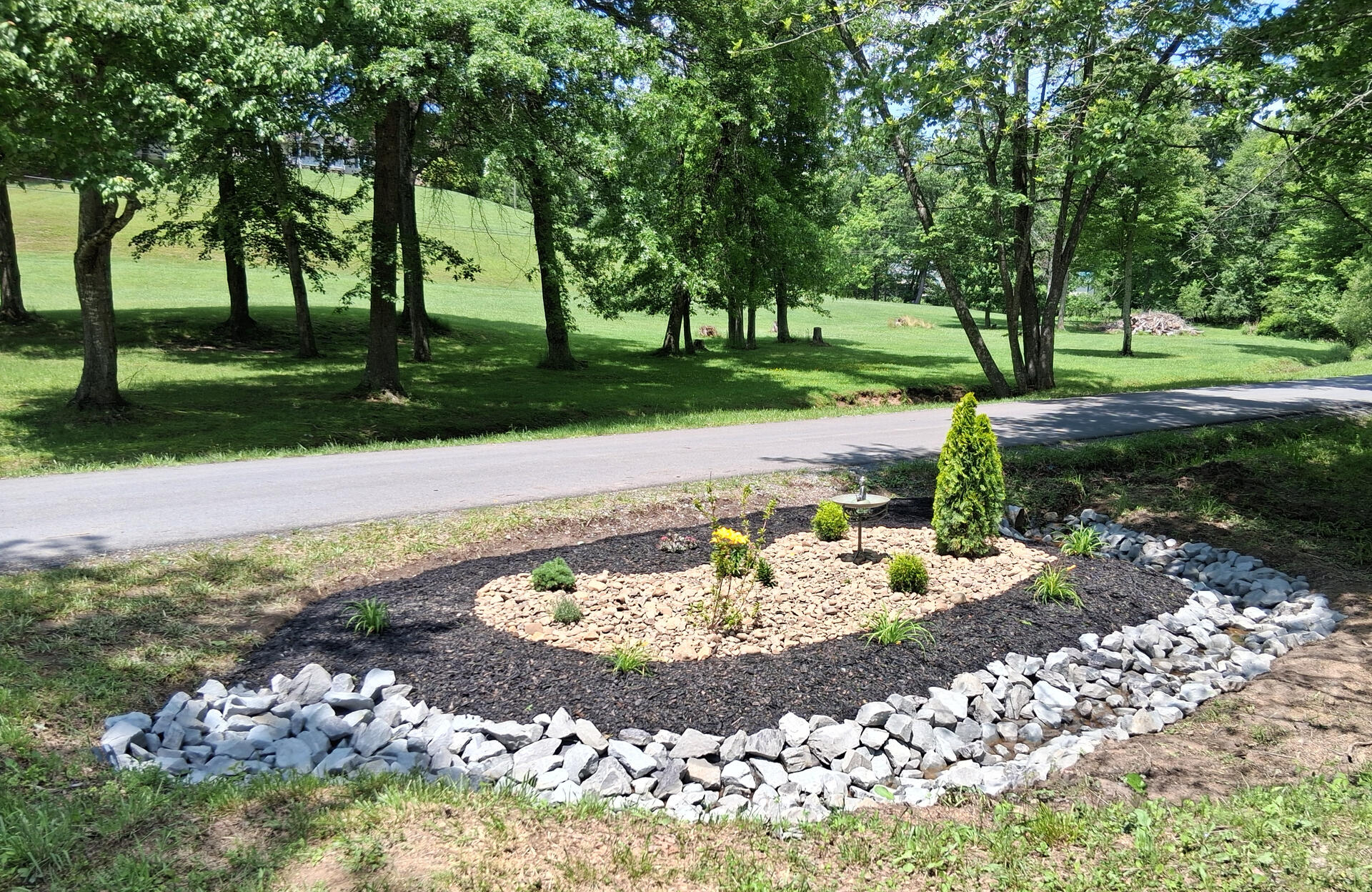 Newly designed and installed luxury landscaped garden bed with large drainage rocks, black mulch, designer river stone, and designer plants with copper buddha bird bath in Fairdale, WV 25839